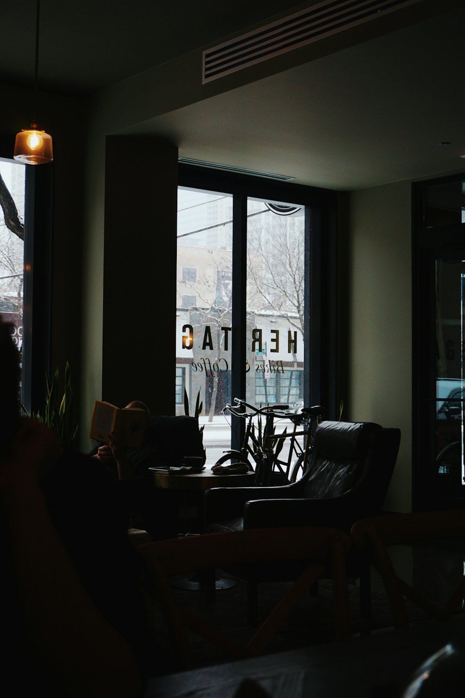 Person reading in armchair at cafe with snow outside.
